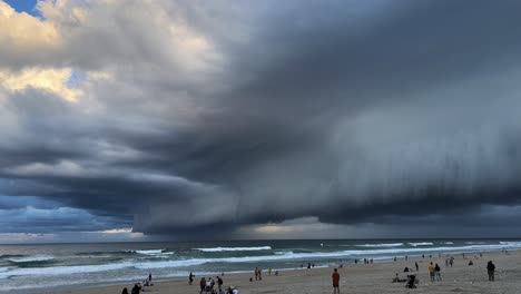 gente en la playa en el paraíso de los surfistas, observando la dramática y gruesa capa de nubes oscuras en el cielo, el clima severo y extremo que se acerca en la temporada de tormentas en gold coast, queensland, australia