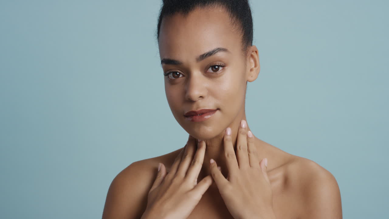 retrato de una hermosa mujer afroamericana tocando el cuerpo con la mano acariciando una piel suave y saludable disfrutando de una belleza natural perfecta con una apariencia confiada sobre un fondo azul concepto de cuidado de la piel