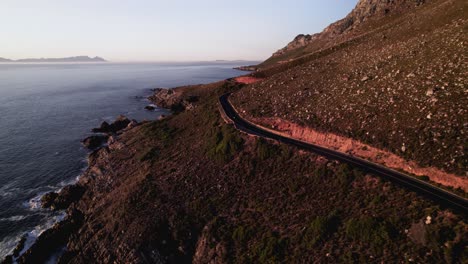 Paseos-En-Motocicleta-Por-La-Costa-Al-Atardecer,-Vista-Por-Drones-De-Una-Sinuosa-Carretera-Panorámica