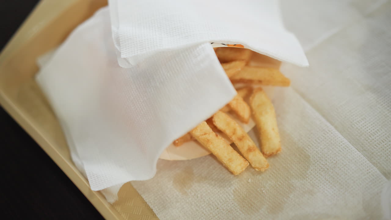 primer plano de papas fritas doradas crujientes parcialmente cubiertas con una servilleta en una bandeja, con una mano alcanzando las papas fritas, la escena captura un momento de cena relajado y casual