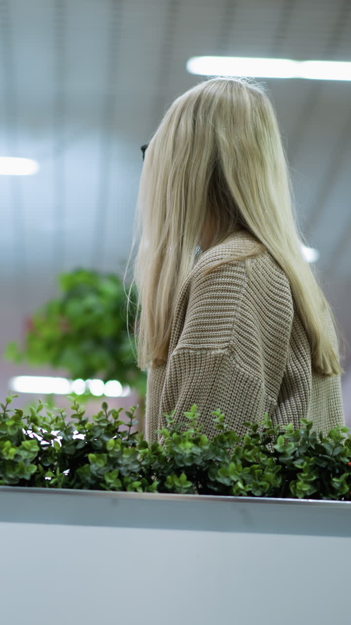 전문적인 여성이 인근의 장식용 식물과 함께 사려 깊게 커피를 마시고, 흐릿한 상점 배경에는 밝은 장식용 불빛이 박이고 있습니다.