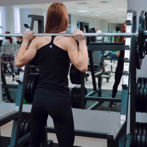 a slender girl in black sportswear raises the barbell and crouches with it on the background of a mirror in a fitness club. healthy lifestyle
