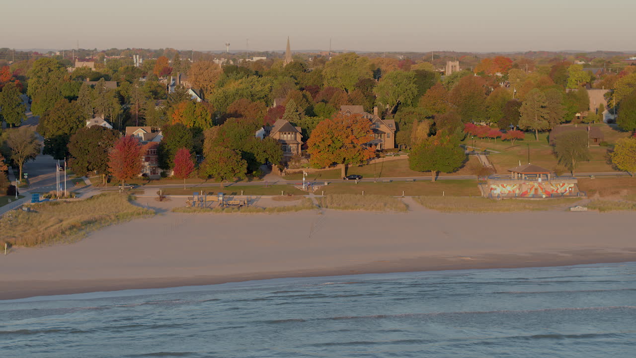 Drone aerial in autumn over Lake Michigan with a slow push toward Sheboygan, Wisconsin shoreline showing a pretty neighborhood with houses and colorful fall trees