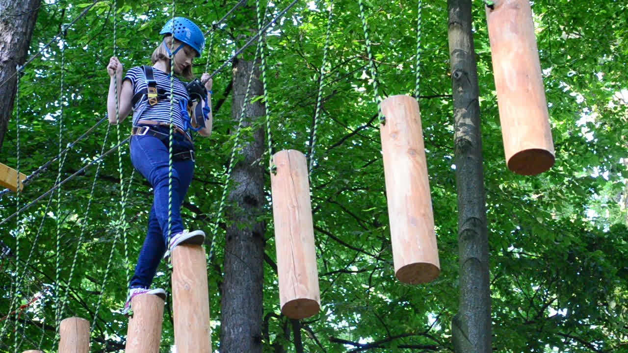 La ragazza adolescente supera ostacoli tra gli alberi in altezza. Riprese in estate