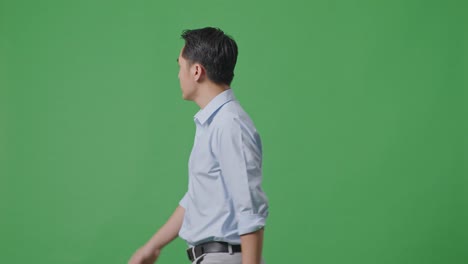 side view of asian business man walking and looking around on green screen background in the studio