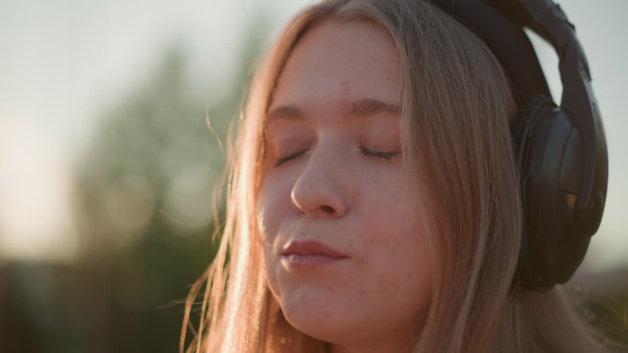 Donna caucasica con cuffie che balla per strada e mangia uno snack, ritratto all'aperto di giovane donna lentigginosa che si scatena sul marciapiede, morso giocoso mentre annuisce a ritmo di musica, luce solare che crea un alone, atmosfera energica ma tranquilla