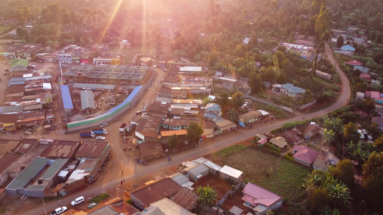Veduta aerea di un vivace mercato rurale a Embu, Kenya, illuminato da una calda luce serale, che mostra negozi, strade, attività commerciali, veicoli, foresta pluviale e attività commerciale in una comunità agricola