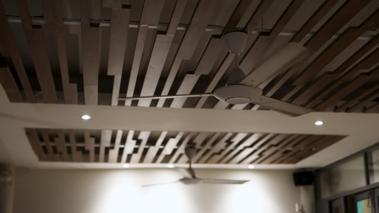 un ventilador de techo gira en una habitación elegante y moderna con pizarras de madera y iluminación suave, creando una atmósfera tranquila