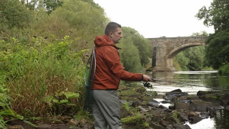 panning shot of a fisherman casting and reeling in his lure at a stream