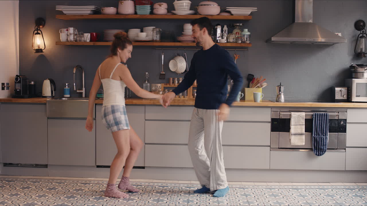 Happy young couple newly wed dancing listening to music in kitchen wearing pajamas morning at home