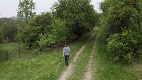 Follow-through-drone-shot-of-a-tourist-walking-on-a-countryside-road-between-the-trees-in-the-village-of-Tsarichina-Hole-in-Bulgaria