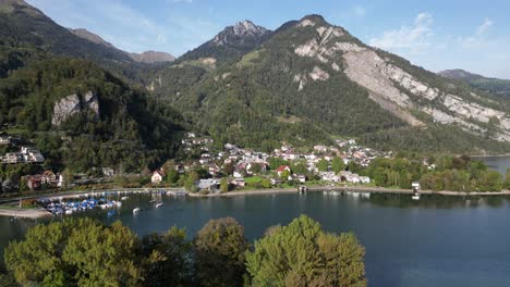 an aerial view of walensee shows a small marina and residential houses with the majestic green swiss alps in the background on a sunny day