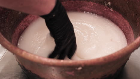 Mano-En-Guantes-Negros-Mezclando-Azúcar-Y-Agua-En-Un-Recipiente