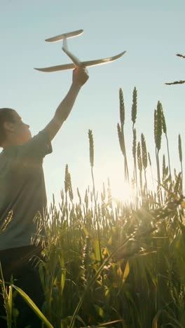boy playing with a toy airplane in a wheat field at sunset