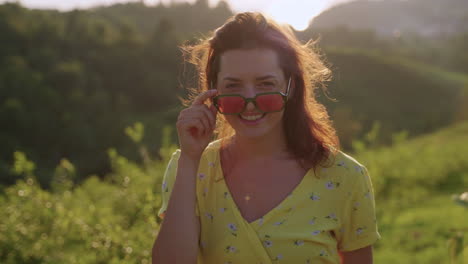 mujer en un vestido amarillo con gafas de sol rosas disfrutando de la puesta de sol
