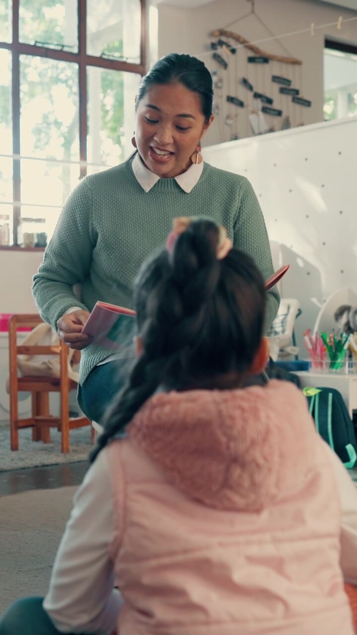 Teacher Reading a Book to a Young Student in a Classroom