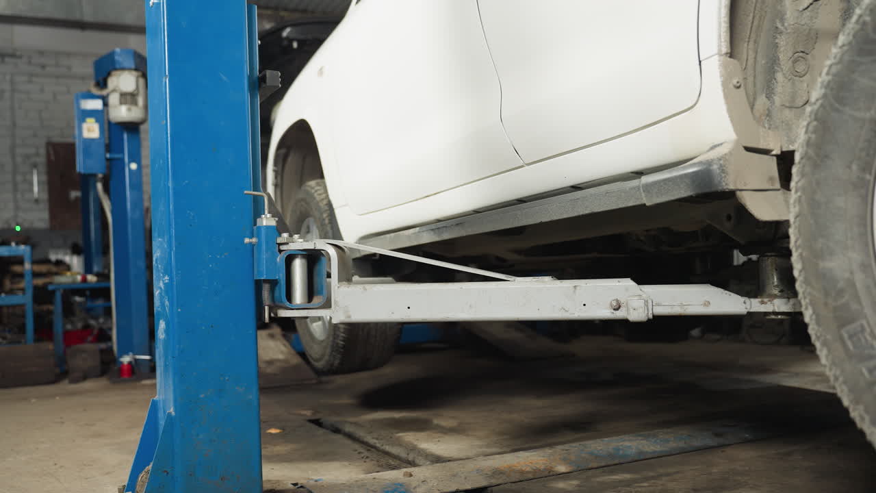 차고에서 자동차 하이드라릭 엘리베이터에 의해 천천히 들어올려지는 색 자동차, 파란색 산업용 자동차 엘리베이트 구조에 의해 지원, 차체와 타이어가 보이고, 기계적 프로세스를 보여줍니다.