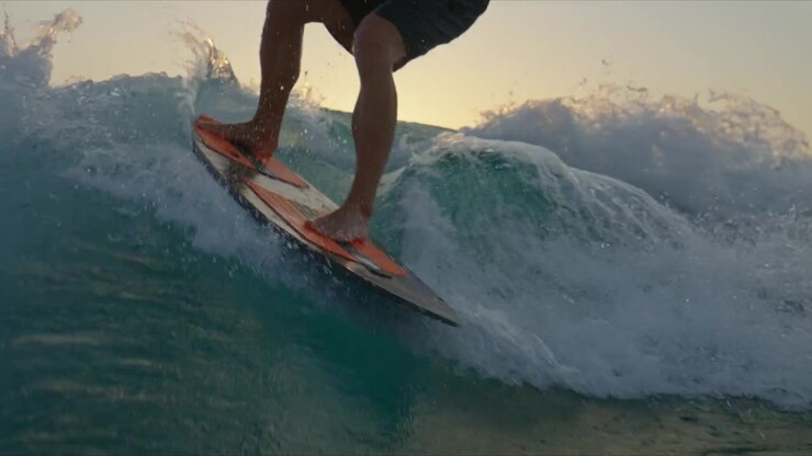 Close up water-level view of a wakesurfer carving through the boat wake. Water spray, surfboard movement and dynamic action create an immersive watersports perspective.