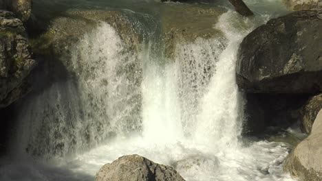 small waterfall of rushing water over rocks in mountain river, slow motion close up