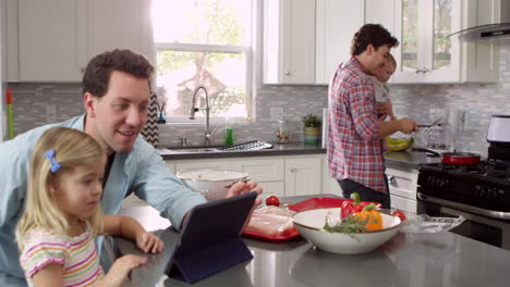 Girl-uses-tablet-in-kitchen-with-parents,-dad-holding-baby