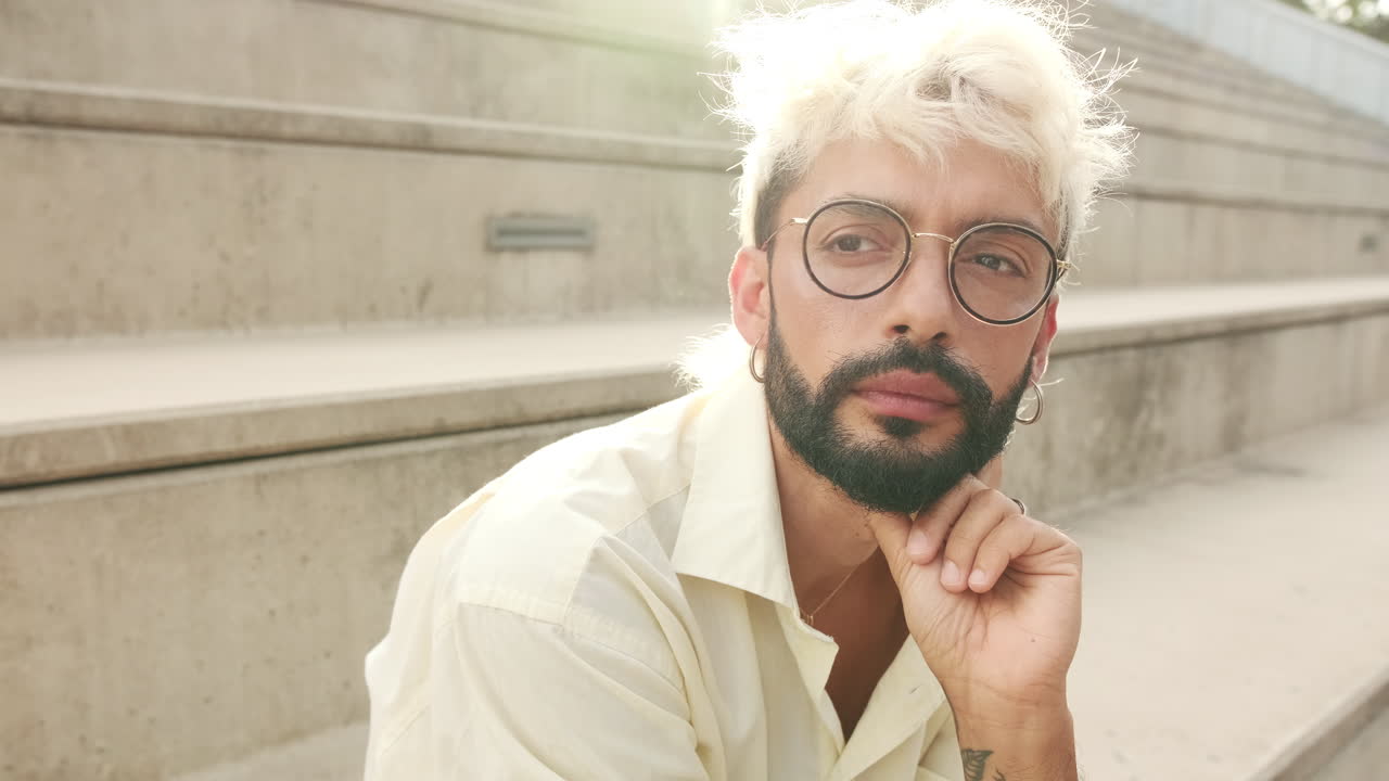 Homem pensativo com cabelo loiro e barba sentado ao ar livre