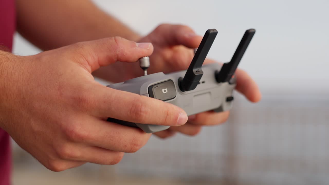 Close-up of hands controlling a drone with a remote on a bright day near the ocean