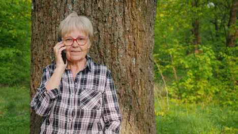 older woman talking on phone near a tree in a forest