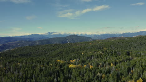 aerial moving over forest with changing aspens and mountains in distance, 4k