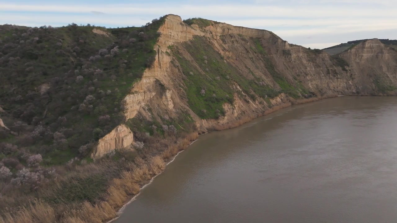 Filmato aereo con drone che mostra una svolta a destra dalla terra verso un'ampia ansa del fiume Tago, rivelando un ripido pendio verticale con scarsa vegetazione verde e acqua torbida.