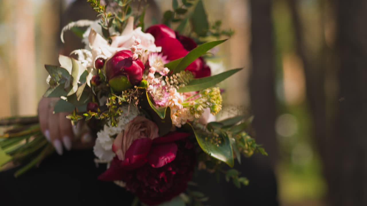 La mano della sposa con il bouquet abbraccia il collo dell'uomo in un parco verde.