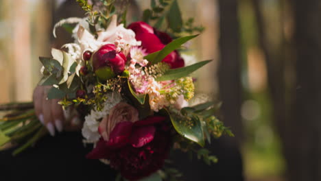 bride hand with bouquet hugs neck of man in green park