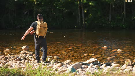 un joven excursionista arrojando una roca rebotando en el río dentro del bosque en cámara lenta