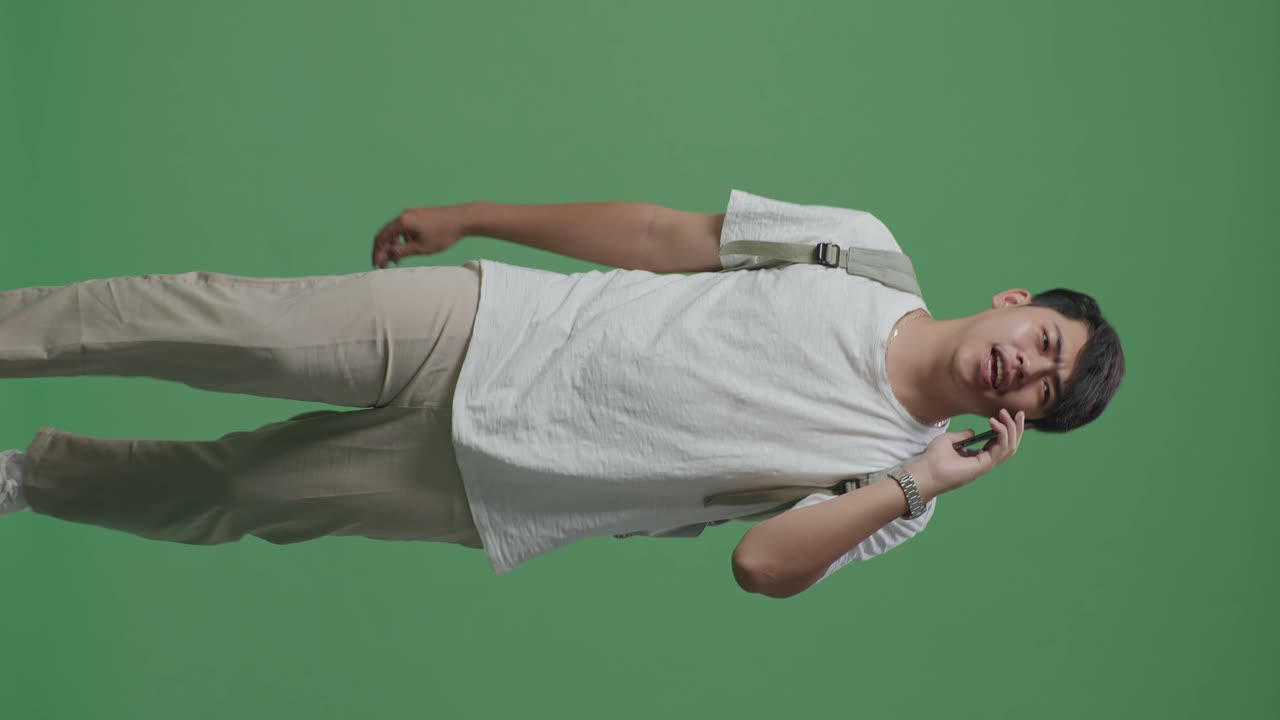 아시아인 학생이 녹색 스크린 스튜디오에서 는 동안 휴대전화로 이야기하고 있습니다.