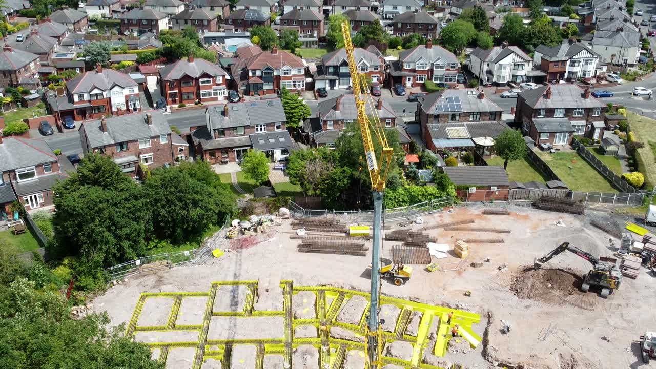 Tall crane setting building foundation in British town neighbourhood aerial view establishing suburban townhouse rooftops