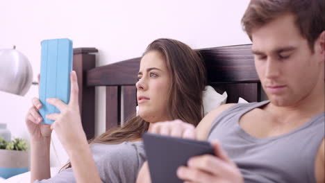 una pareja joven usando una tableta digital en la cama.