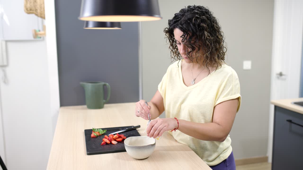 Woman adding sugar to strawberries in modern kitchen
