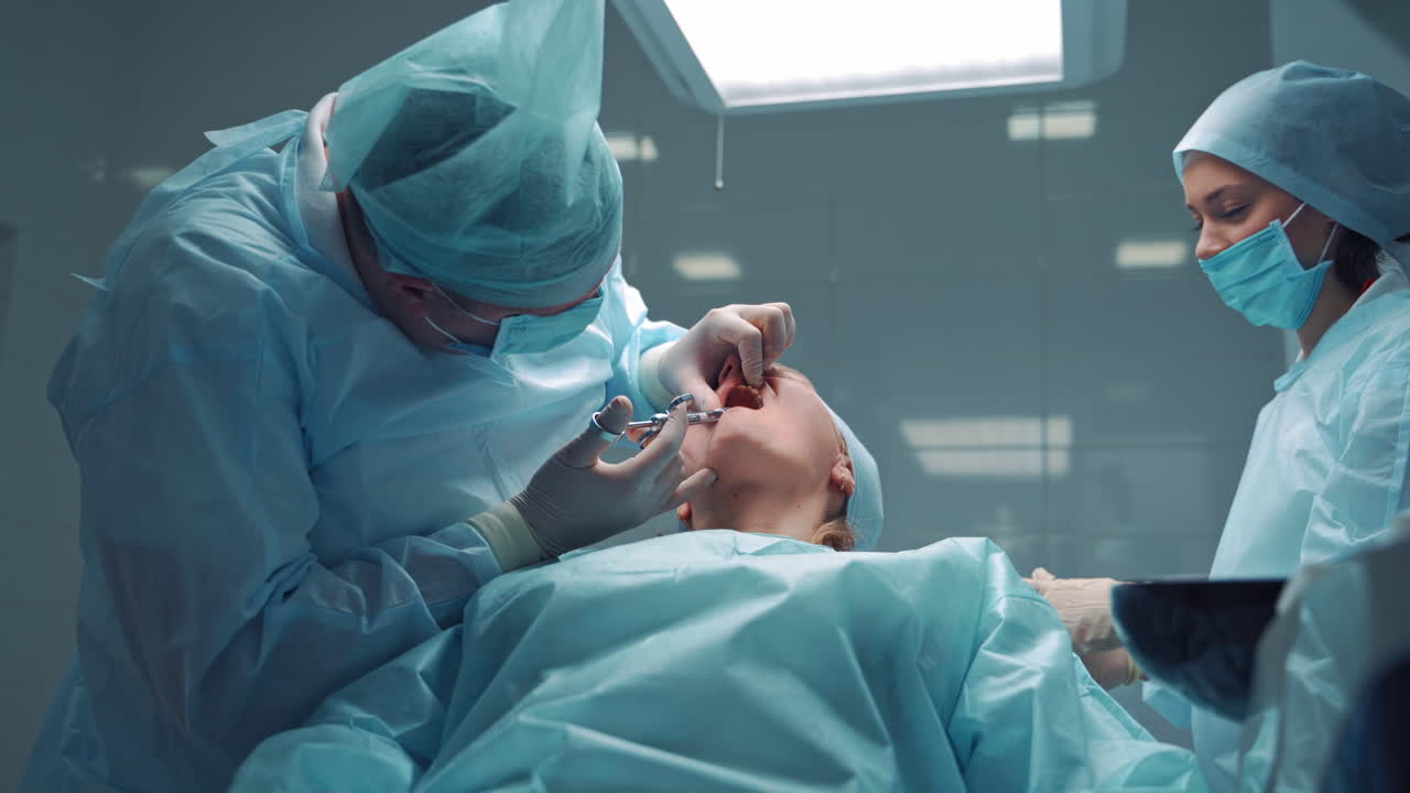 Stomatologist man in special clothes is doing anesthetic injection into the client's mouth. Doctor dentist and his assistant prepare the patient for tooth treatment in dental office.