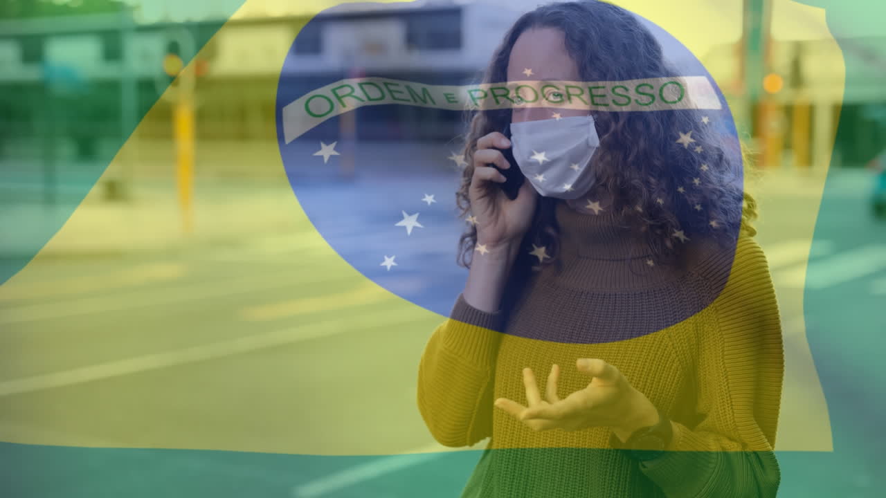 bandera brasileña ondeando contra una mujer que usa una máscara facial hablando en un teléfono inteligente