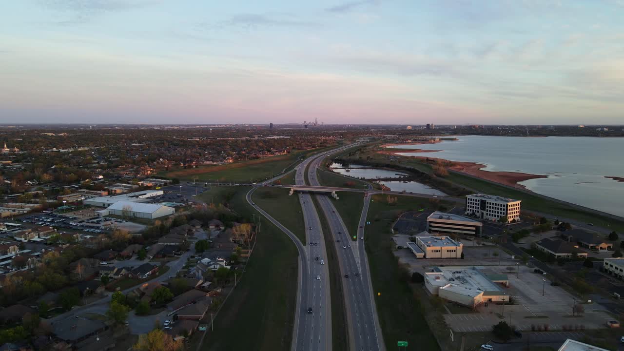 Aerial view of a highway intersecting an urban landscape with a lake at sunset or sunrise