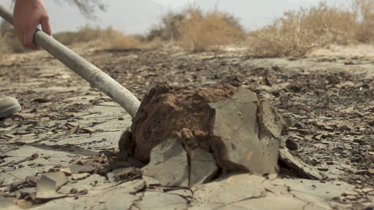 Uomo che scava terreno secco con una pala di giorno nel deserto, primo piano.