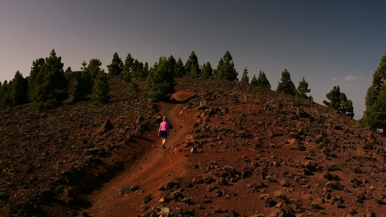 Aerial shot of a woman going up a trail in a volcanic landscape in a sunny day