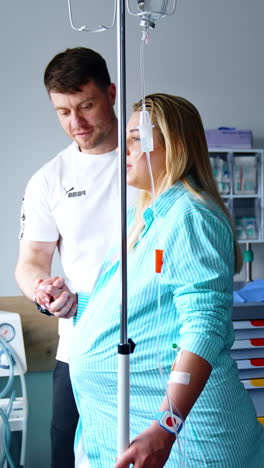 blonde caucasian woman expecting a child is in the hospital room. pregnant lady walks supported by her husband and looks at window. vertical video