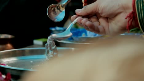 Close-up-of-hands-pouring-water-over-Lord-Ganesh-during-wedding-puja