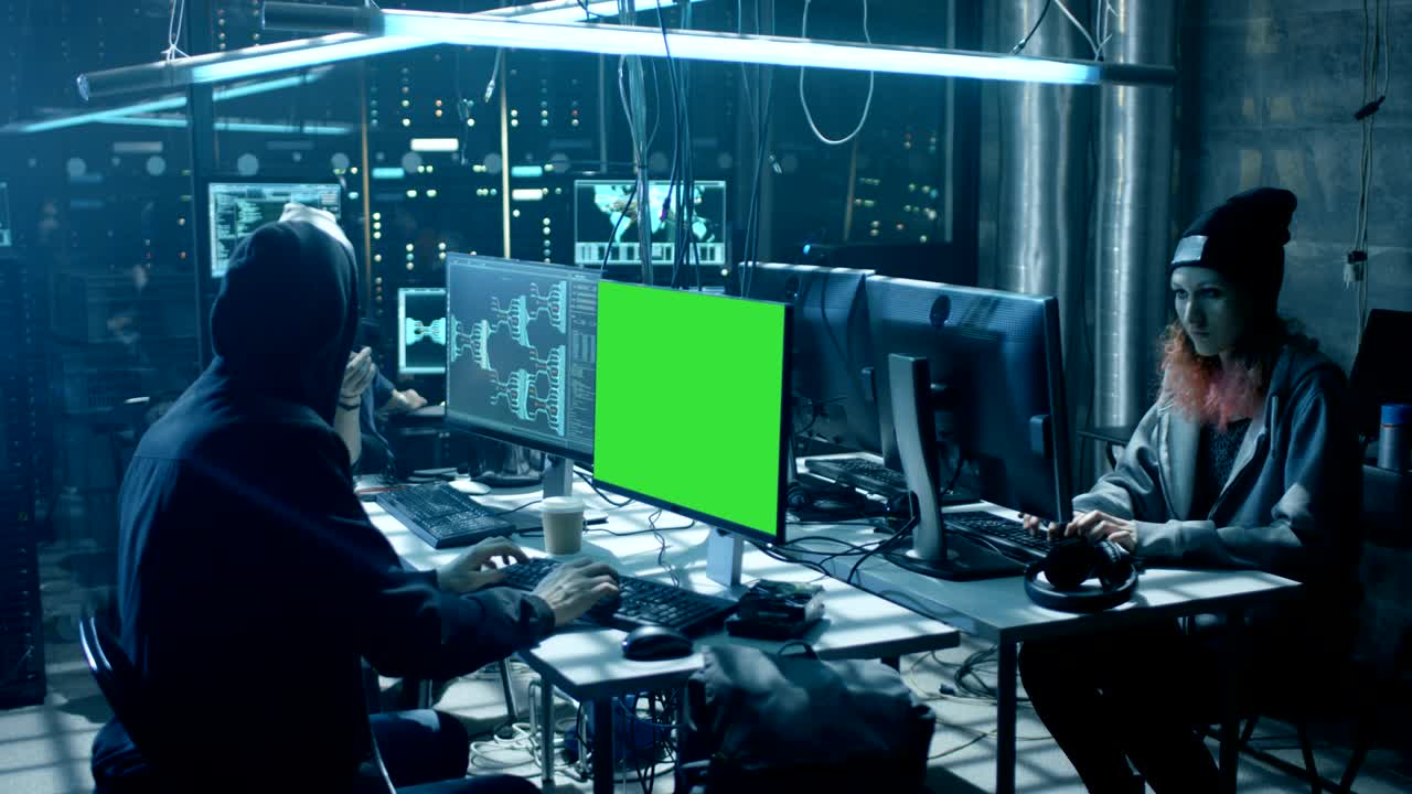 un equipo de hackers adolescentes buscados internacionalmente con pantalla verde infectan servidores e infraestructura con virus. su escondite es oscuro, iluminado con neón y tiene múltiples pantallas.