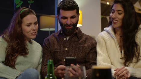 group of friends dressing up at home or in bar celebrating at st patrick's day party posing for selfie on phone