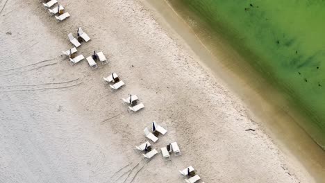 로즈메리 비치 (rosmery beach) 에 모래로 오는 파도와 함께 빈 라운지 의자 (lounge chairs) 에 가까운 슬라이딩 대각선 시각