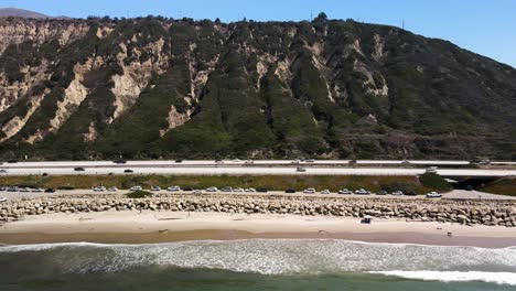 lateral aerial shot of cars on pch next to the beach in california