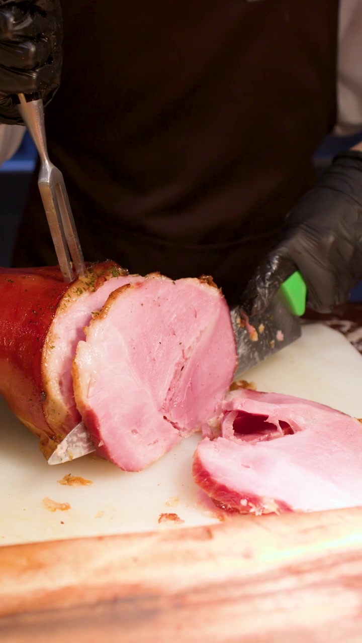Primo piano di uno chef che affetta fette sottili di prosciutto arrosto usando un coltello da intaglio affilato.