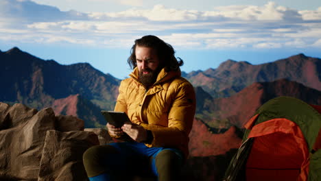 camper fighting the strong wind while he uses tablet at high altitude campsite