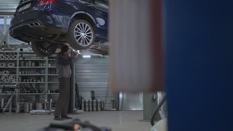 Plan-General-El-Mecánico-Inspecciona-El-Sistema-De-Escape-Del-Coche-En-El-Servicio-De-Coches.-Coche-En-El-Ascensor-Inspección-Y-Diagnóstico-De-Problemas-Con-La-Suspensión-Del-Coche